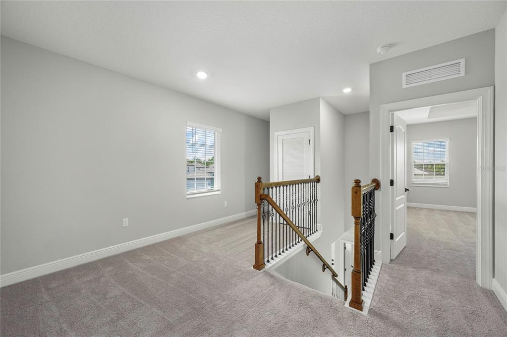 A carpeted upstairs landing features a wooden staircase with iron railings and two doorways — 7657 SOMERSWORTH DRIVE, KISSIMMEE, FL