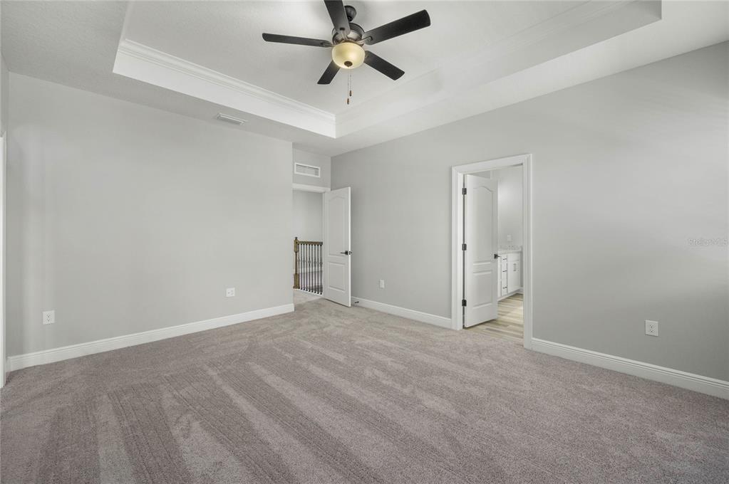 A bedroom with gray carpet, light gray walls, a tray ceiling, and two open doorways — 7657 SOMERSWORTH DRIVE, KISSIMMEE, FL