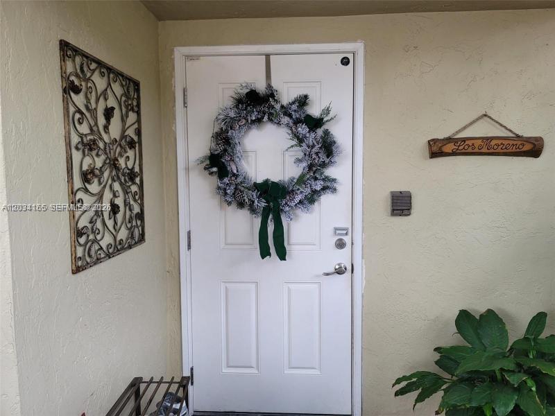 A white front door with a holiday wreath is flanked by a wall decoration and plant — 9673 SW 138th Ave, Miami FL 33186, MIAMI, FL
