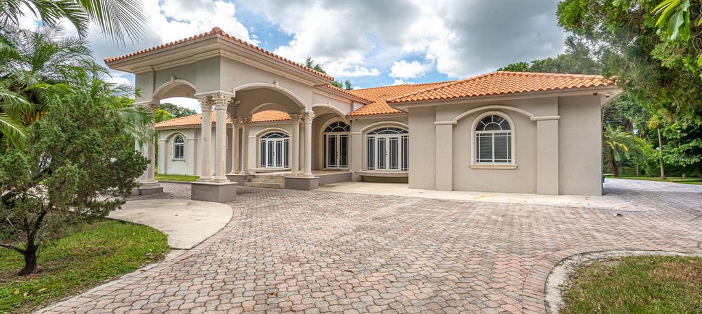 A beige single-story house with a tiled roof, arched windows, and a large stone-columned porte-cochère — 18390 SW 200TH STREET, MIAMI, FL