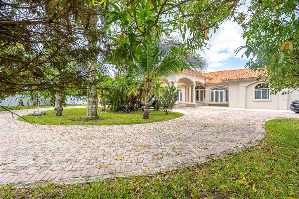 A circular paver driveway leads to the entrance of a single-story house with palm trees — 18390 SW 200TH STREET, MIAMI, FL