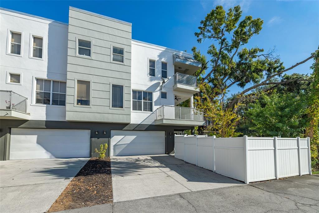 A modern three-story townhouse with white siding, two garage doors, and a white privacy fence — 113 S NEWPORT AVENUE UNIT 1-4, TAMPA, FL