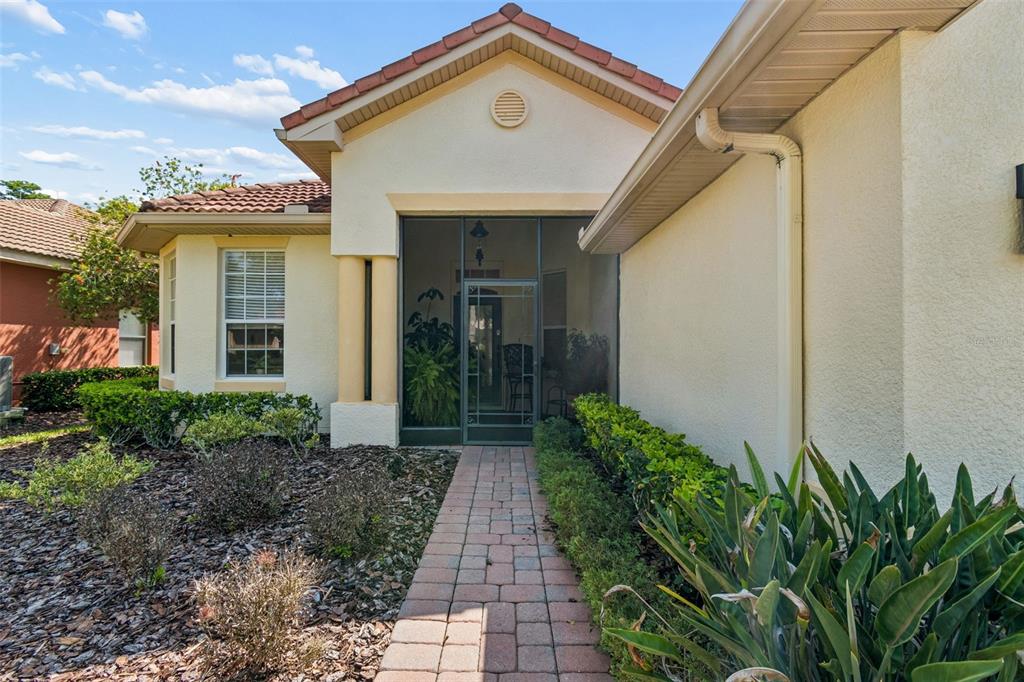A paved walkway leads to the screened-in front entryway of a tan stucco house — 729 CORONADO DRIVE, POINCIANA, FL