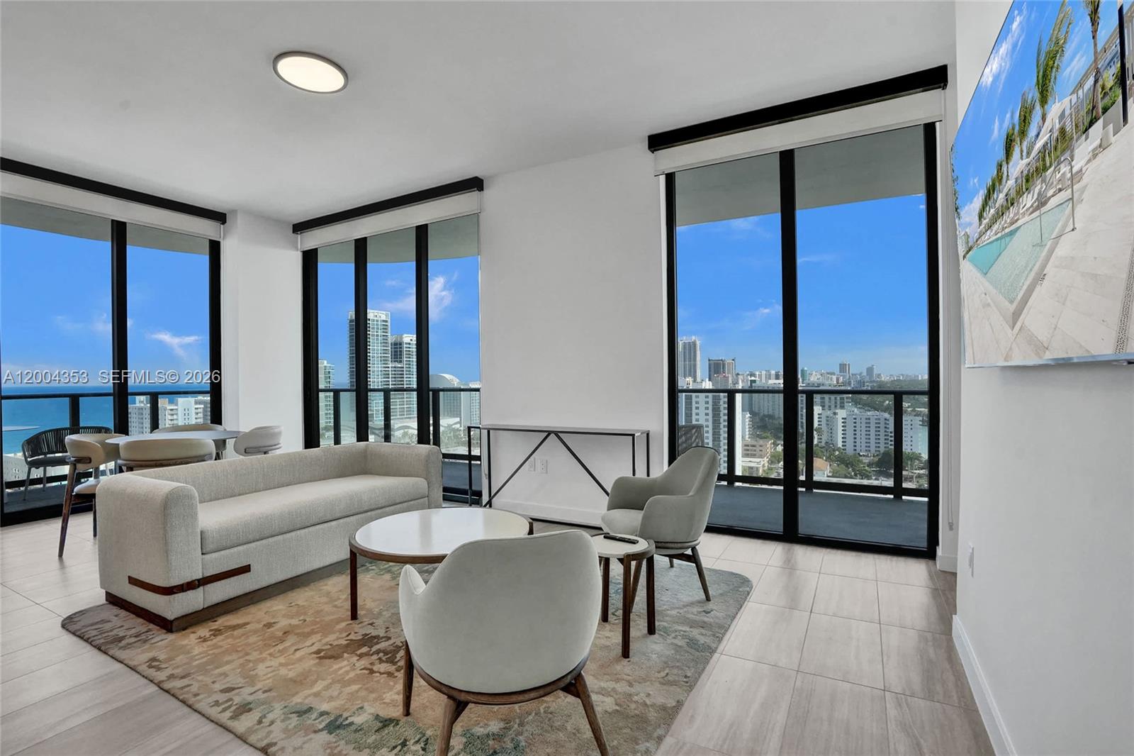 A modern living room features floor-to-ceiling windows, a neutral sofa, and a city view — 580 72nd St # 1702, Miami Beach FL 33141, MIAMI BEACH, FL