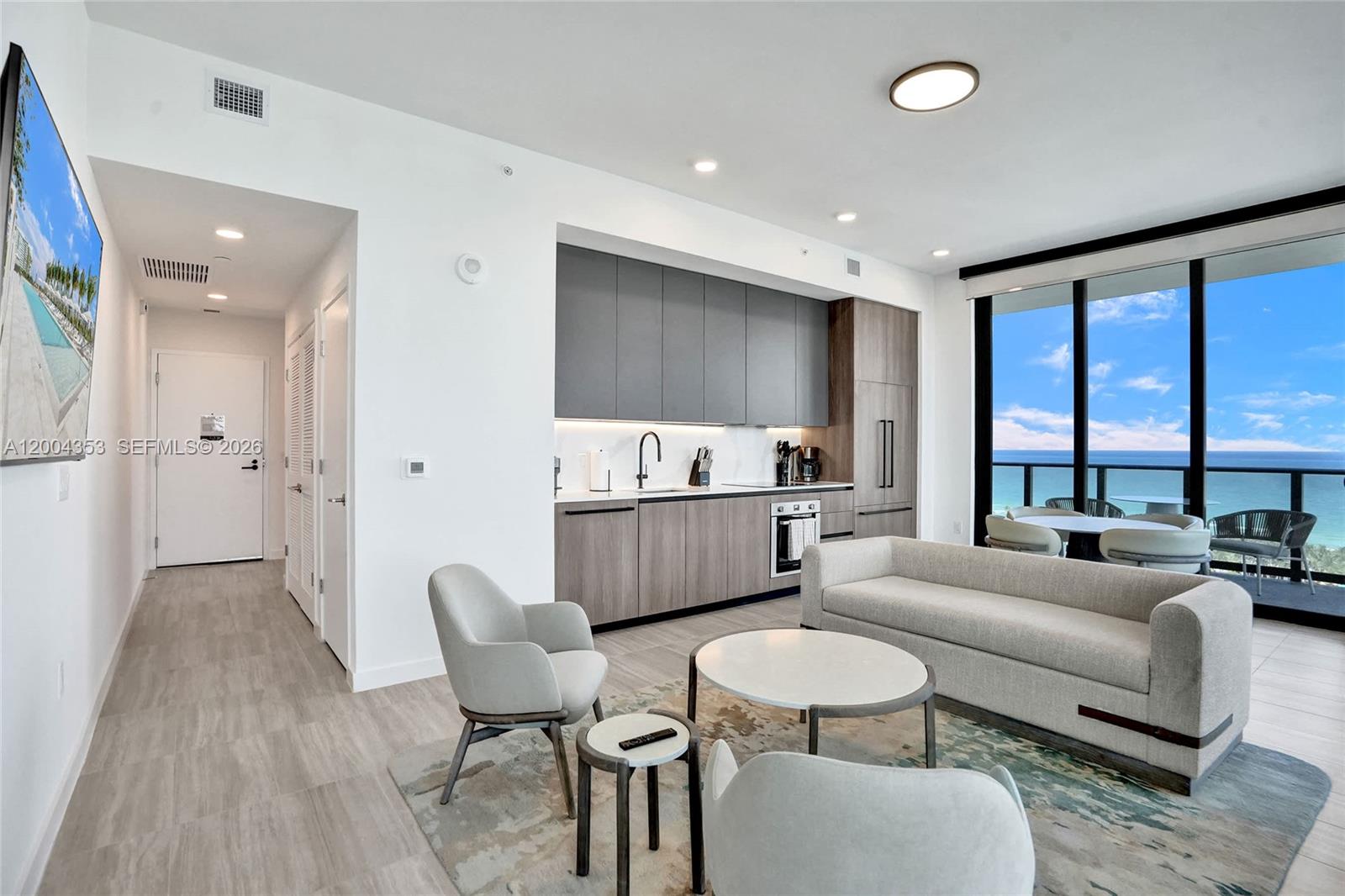 A modern living room and kitchen area features light wood flooring, gray cabinetry, and ocean views — 580 72nd St # 1702, Miami Beach FL 33141, MIAMI BEACH, FL