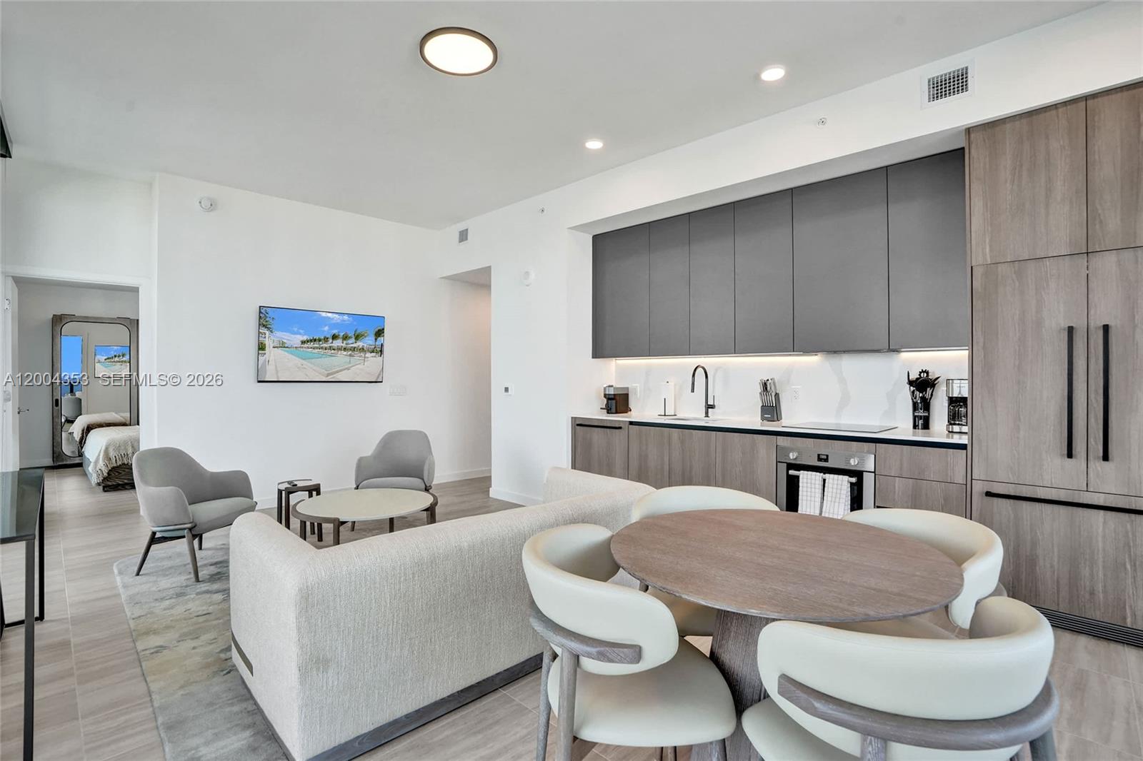 A modern open-concept living area features a kitchen with gray cabinets and a dining table — 580 72nd St # 1702, Miami Beach FL 33141, MIAMI BEACH, FL
