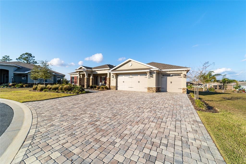 A single-story suburban house with a stone facade, covered entryway, and three-car garage at sunset — 10453 SW 99TH LANE, OCALA, FL