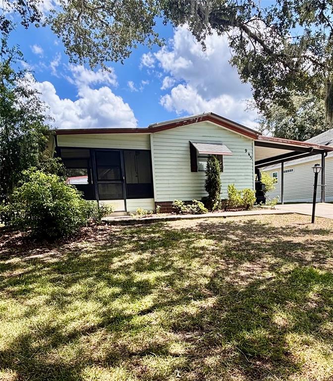 A light-colored house with a screened-in porch and an attached carport sits on a lawn — 945 TARRSON BOULEVARD, LADY LAKE, FL