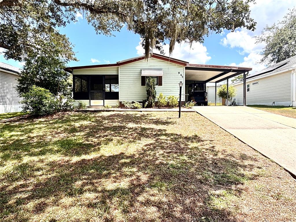A single-story house with light siding, a screened porch, and a carport over a driveway — 945 TARRSON BOULEVARD, LADY LAKE, FL