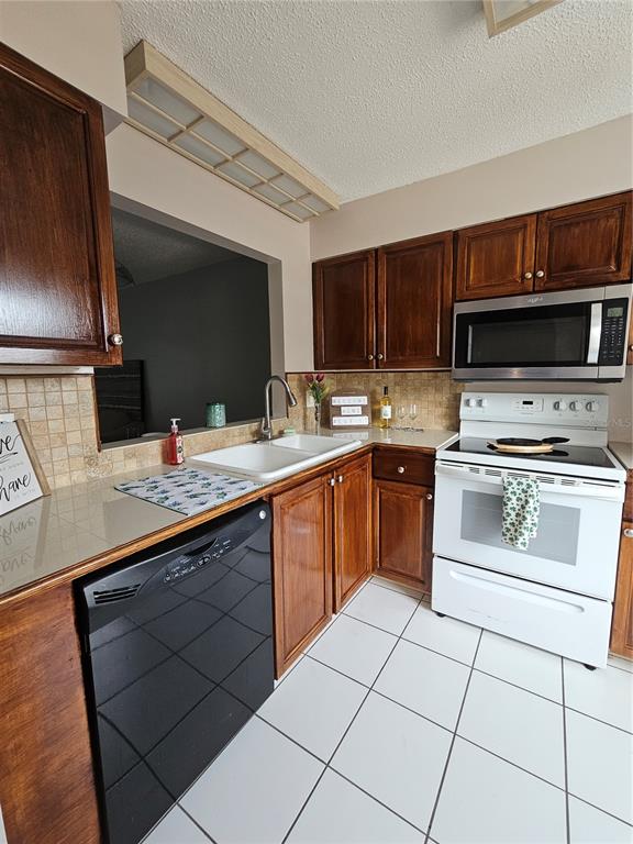 A kitchen features dark wood cabinets, white appliances, a black dishwasher, and white tile flooring — 13813 MISSION OAKS BOULEVARD, SEMINOLE, FL