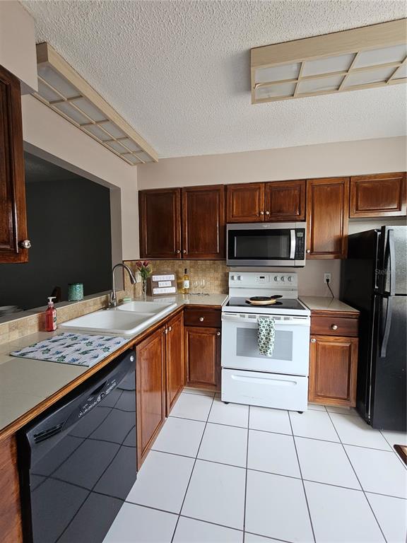 A kitchen features dark wood cabinets, white tile floors, and black appliances — 13813 MISSION OAKS BOULEVARD, SEMINOLE, FL