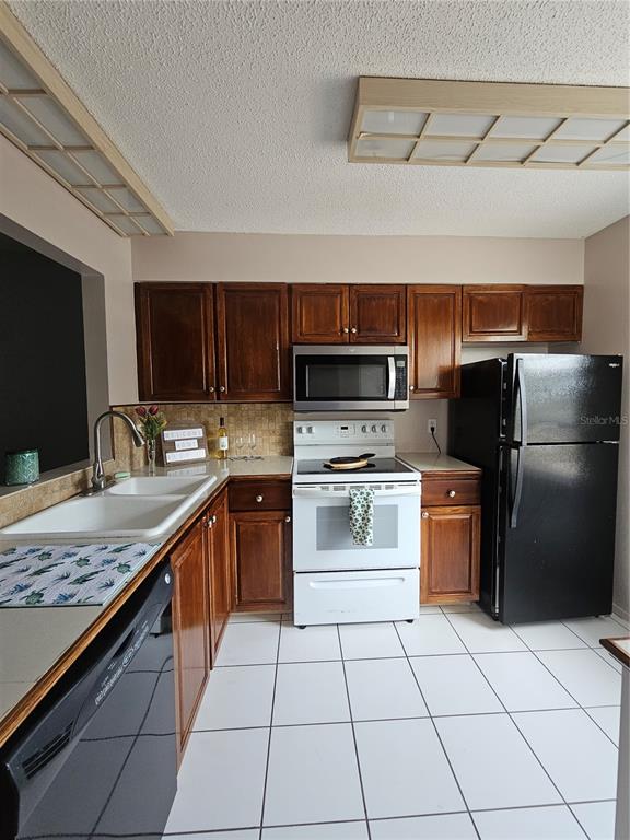 A kitchen features dark wood cabinets, white appliances, a black refrigerator, and white tile flooring — 13813 MISSION OAKS BOULEVARD, SEMINOLE, FL