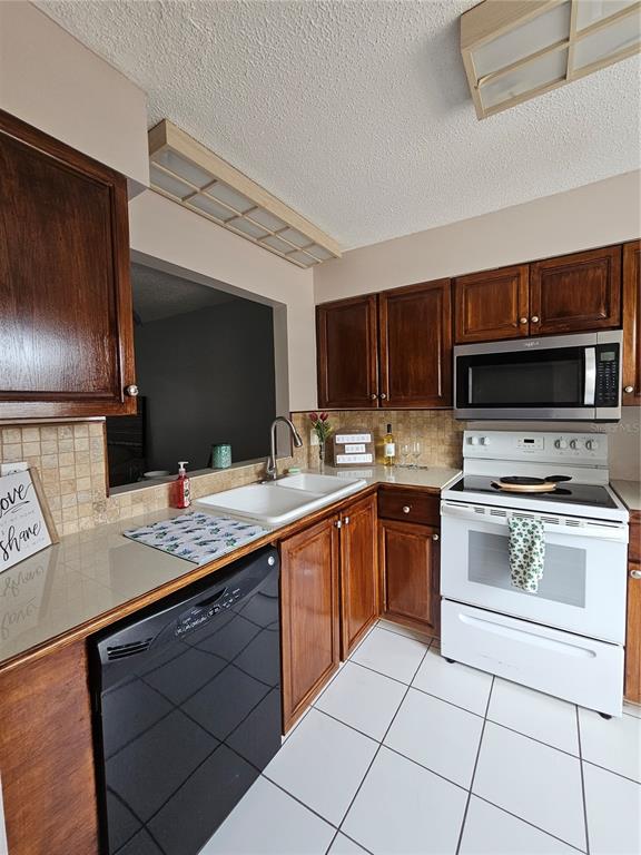 A kitchen features dark wood cabinets, white appliances, a double sink, and white tile flooring — 13813 MISSION OAKS BOULEVARD, SEMINOLE, FL