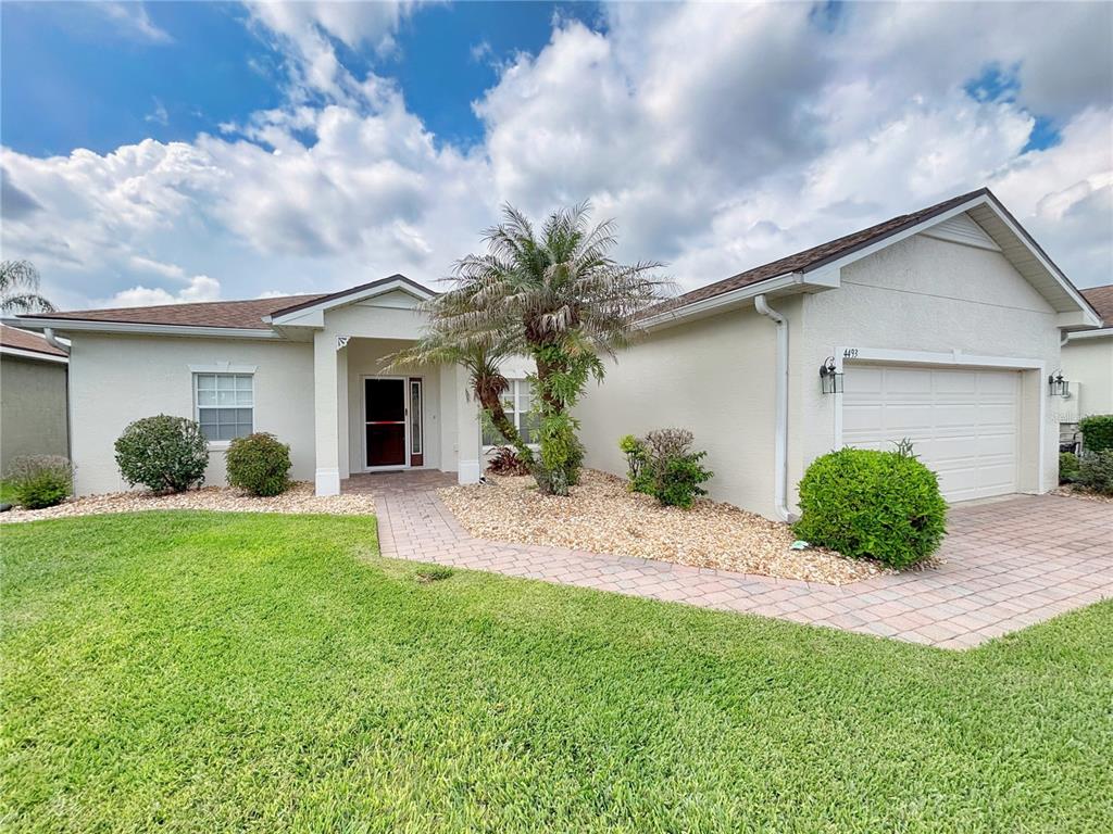 A single-story house with a beige stucco exterior, a palm tree, and a paved driveway — 4493 TURNBERRY LANE, LAKE WALES, FL