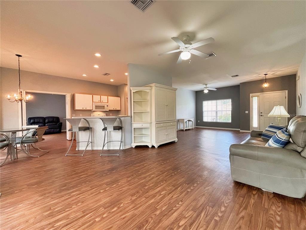 An open-concept living area features wood-look flooring, a kitchen with a breakfast bar, and ceiling fans — 4493 TURNBERRY LANE, LAKE WALES, FL