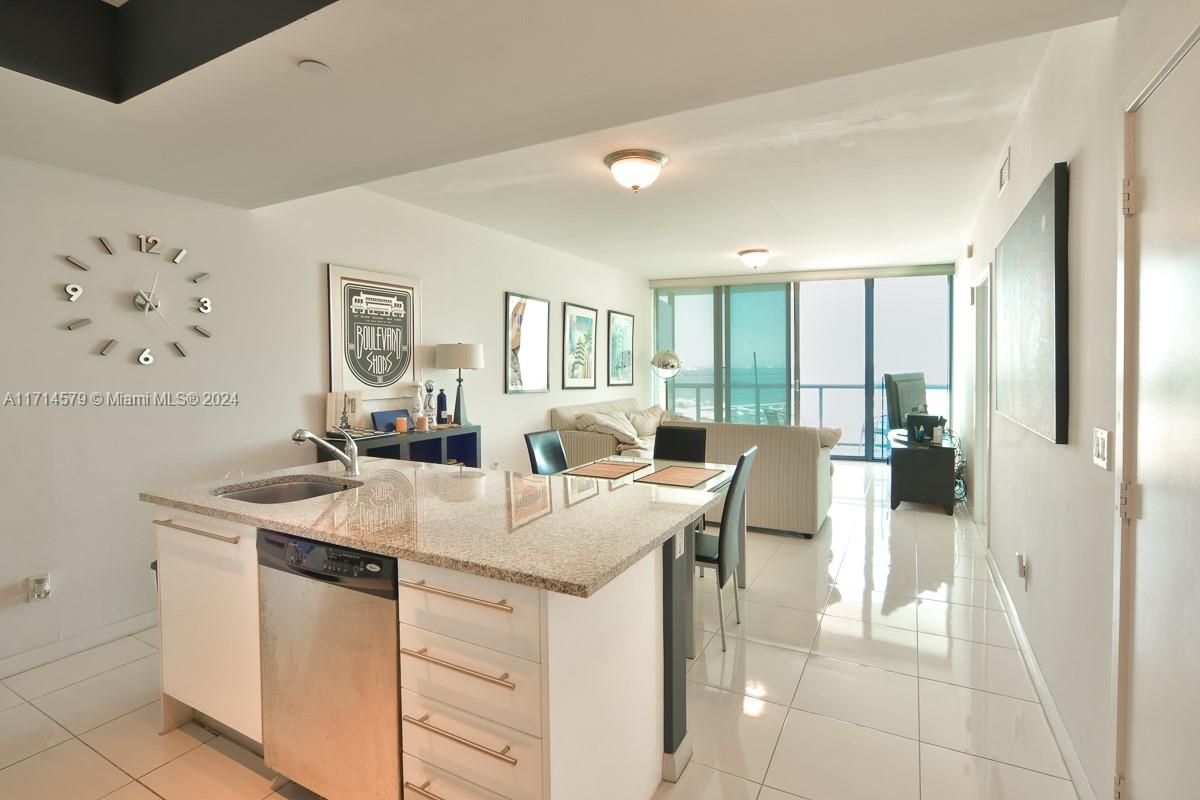 A modern kitchen island with granite countertops overlooks a living area with floor-to-ceiling windows — 888 Biscayne Blvd # 2511, Miami FL 33132, MIAMI, FL