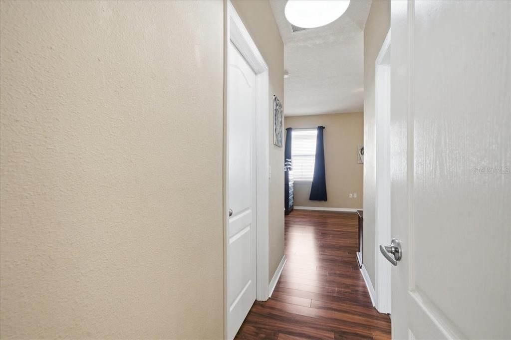 A hallway with wood-look flooring leads to a bedroom with a window and dark curtains — 11844 COLONY LAKES BOULEVARD, NEW PORT RICHEY, FL