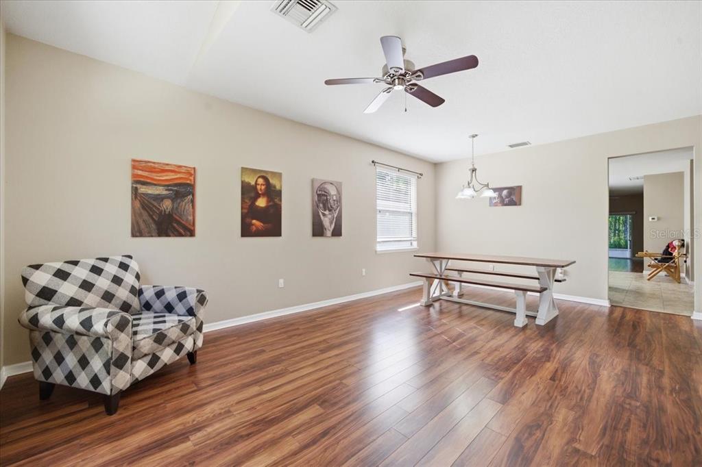 A dining room with wood-look flooring, a ceiling fan, a picnic-style table, and wall art — 11844 COLONY LAKES BOULEVARD, NEW PORT RICHEY, FL
