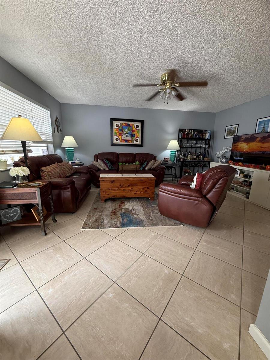 A living room with tile flooring, leather furniture, a wooden coffee table, and a ceiling fan — 462 Normandy J, Delray Beach FL 33484, DELRAY BEACH, FL