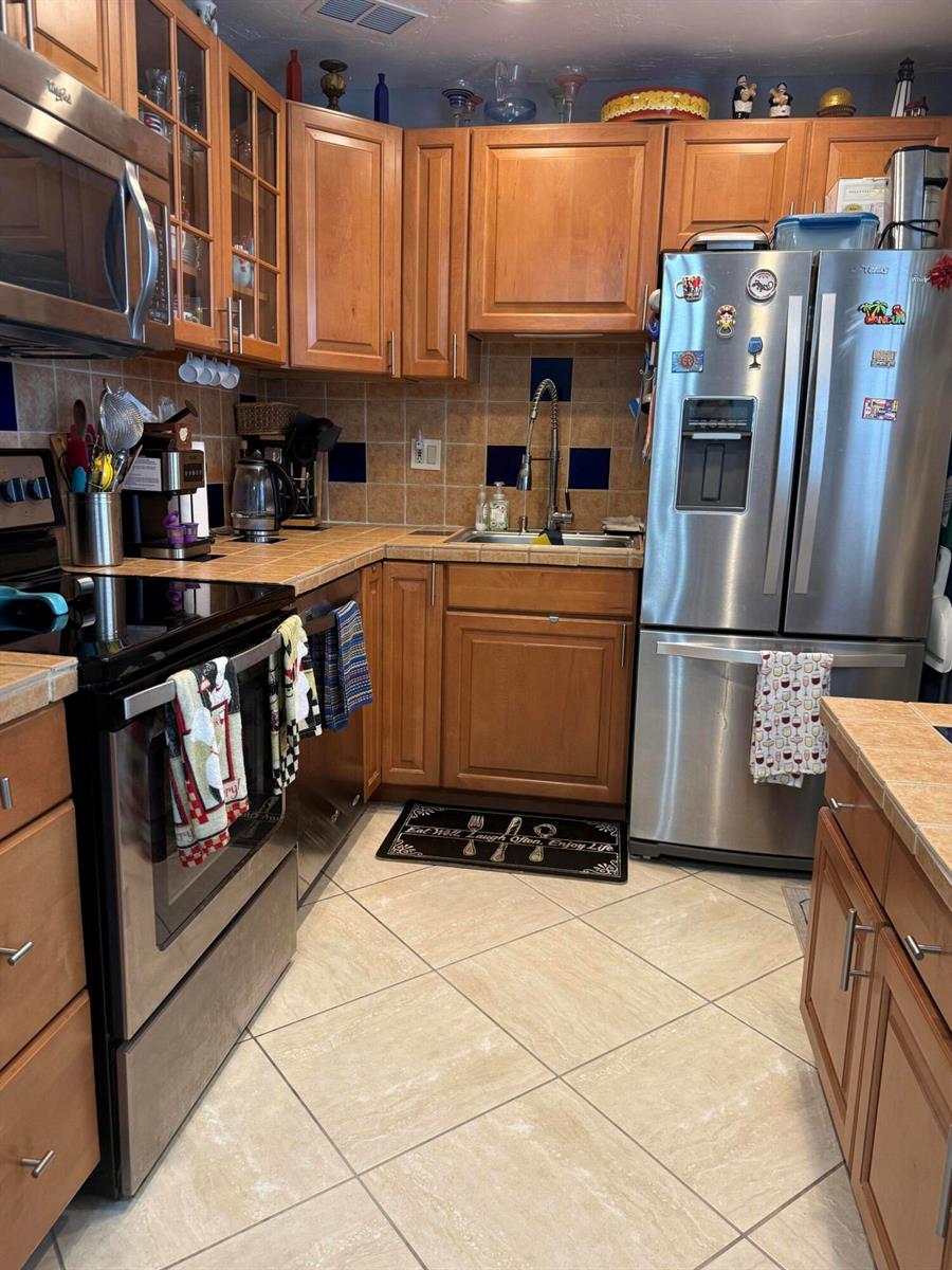 A kitchen features wood cabinets, stainless steel appliances, tile countertops, and a tile floor — 462 Normandy J, Delray Beach FL 33484, DELRAY BEACH, FL