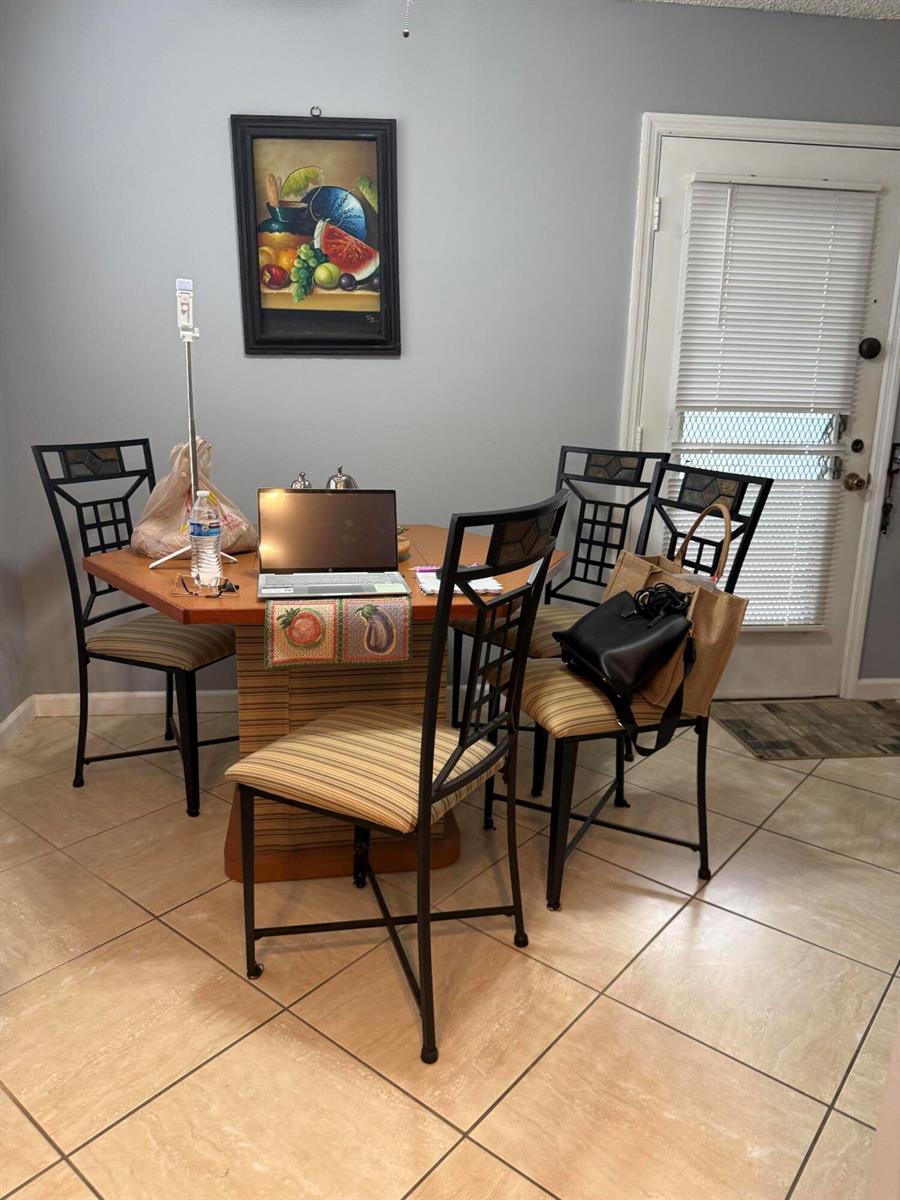 A dining area features a square wooden table with four chairs and a laptop — 462 Normandy J, Delray Beach FL 33484, DELRAY BEACH, FL