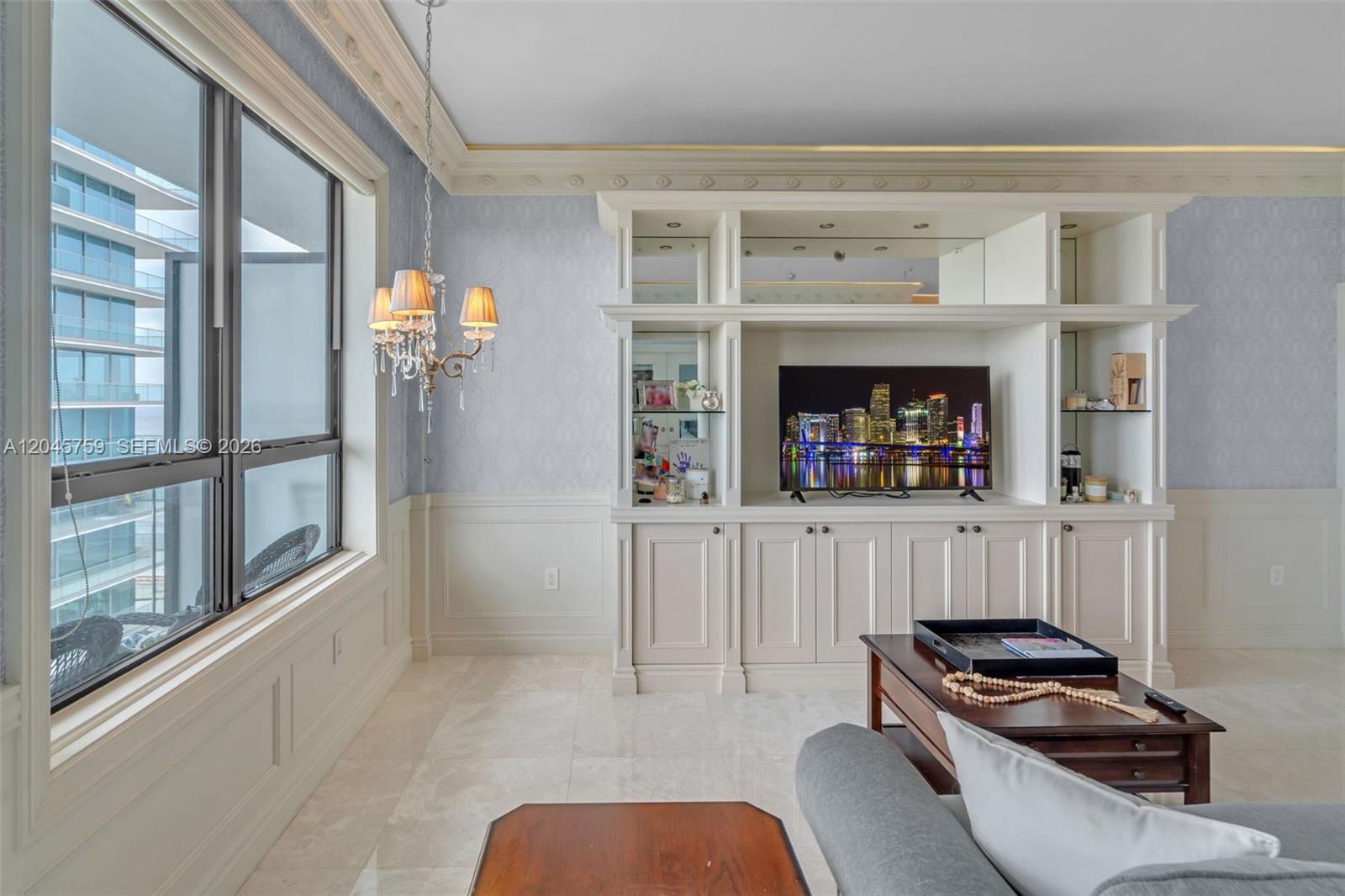 A living room features built-in cabinetry, a television, a chandelier, and large windows with views — 10185 Collins Ave, Bal Harbour FL 33154, BAL HARBOUR, FL