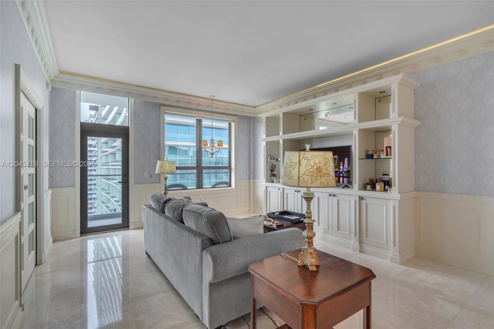 A living room features a gray sofa, built-in cabinetry, and a view of nearby buildings — 10185 Collins Ave, Bal Harbour FL 33154, BAL HARBOUR, FL