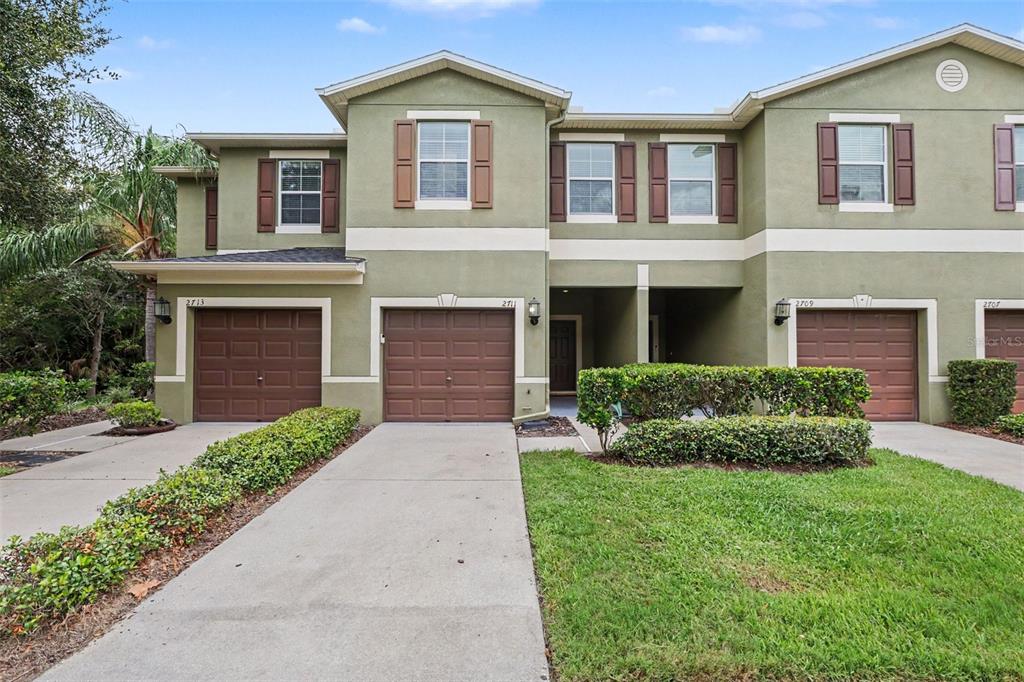 The exterior of a multi-unit townhouse complex features green stucco walls, brown garage doors, and landscaping — 2711 ISABELLA VALLEY COURT, BRANDON, FL