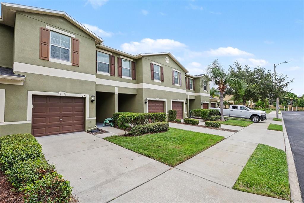 A row of two-story townhomes with green stucco walls, brown garage doors, and concrete driveways — 2711 ISABELLA VALLEY COURT, BRANDON, FL