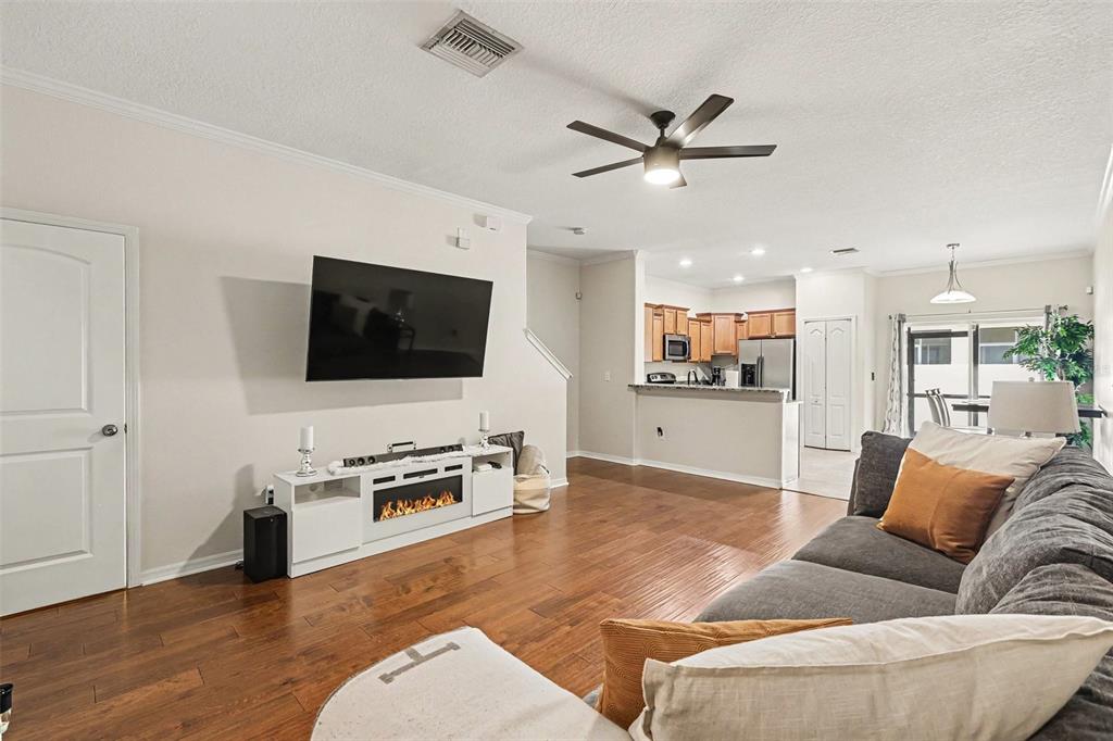 A living room with hardwood floors, a wall-mounted television, and an open kitchen beyond — 2711 ISABELLA VALLEY COURT, BRANDON, FL