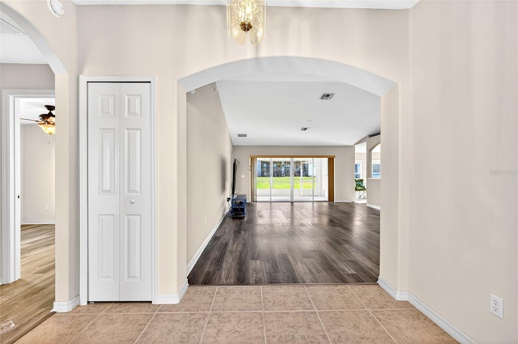 A view through an arched doorway into a living area with wood-look flooring and sliding doors — 1706 SW 156TH LANE, OCALA, FL