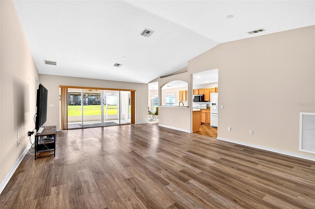 A spacious living room with wood-look flooring, vaulted ceilings, and a sliding glass door — 1706 SW 156TH LANE, OCALA, FL