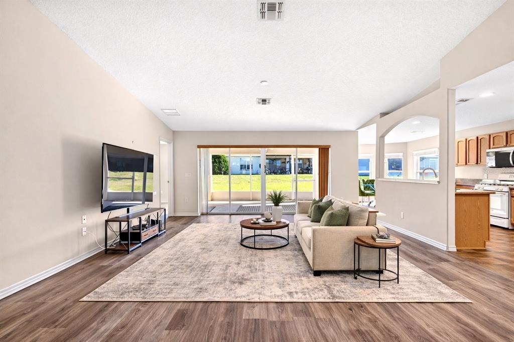 A living room with wood-look flooring, a beige sofa, and sliding glass doors to a patio — 1706 SW 156TH LANE, OCALA, FL