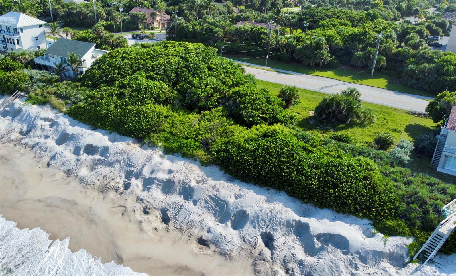 An aerial view shows a sandy beach, dense green vegetation, and nearby coastal residential homes — 7703 S Hwy A1a, Melbourne Beach FL 32951, MELBOURNE BEACH, FL