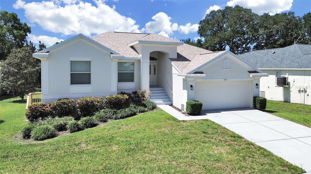 A single-story house with a white stucco exterior, a two-car garage, and a landscaped yard — 1025 LAKE AVOCA PLACE, TARPON SPRINGS, FL