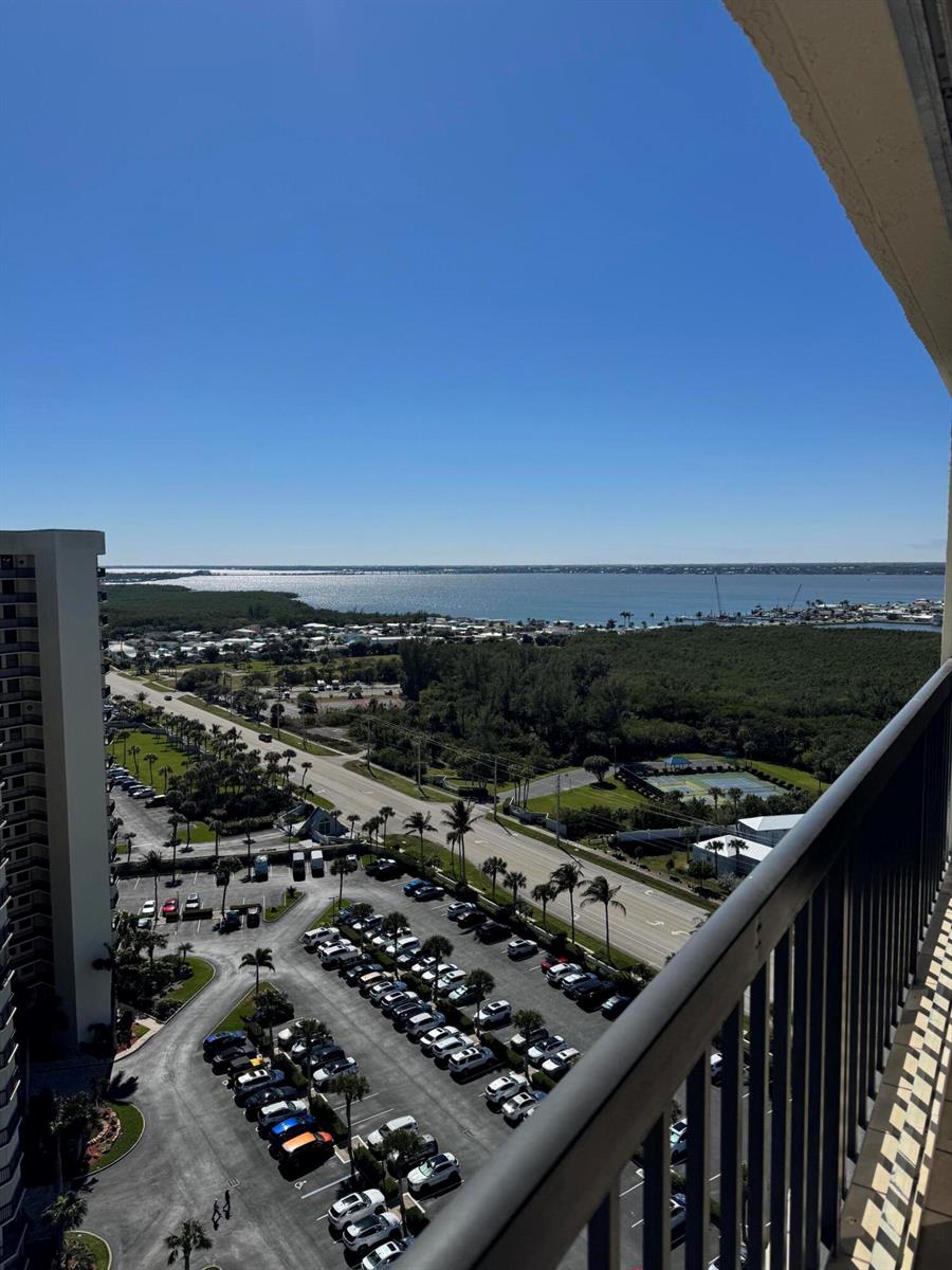A high-angle view from a balcony overlooking a parking lot, road, trees, and water — 9500 S Ocean Drive # 09, Jensen Beach FL 34957, JENSEN BEACH, FL