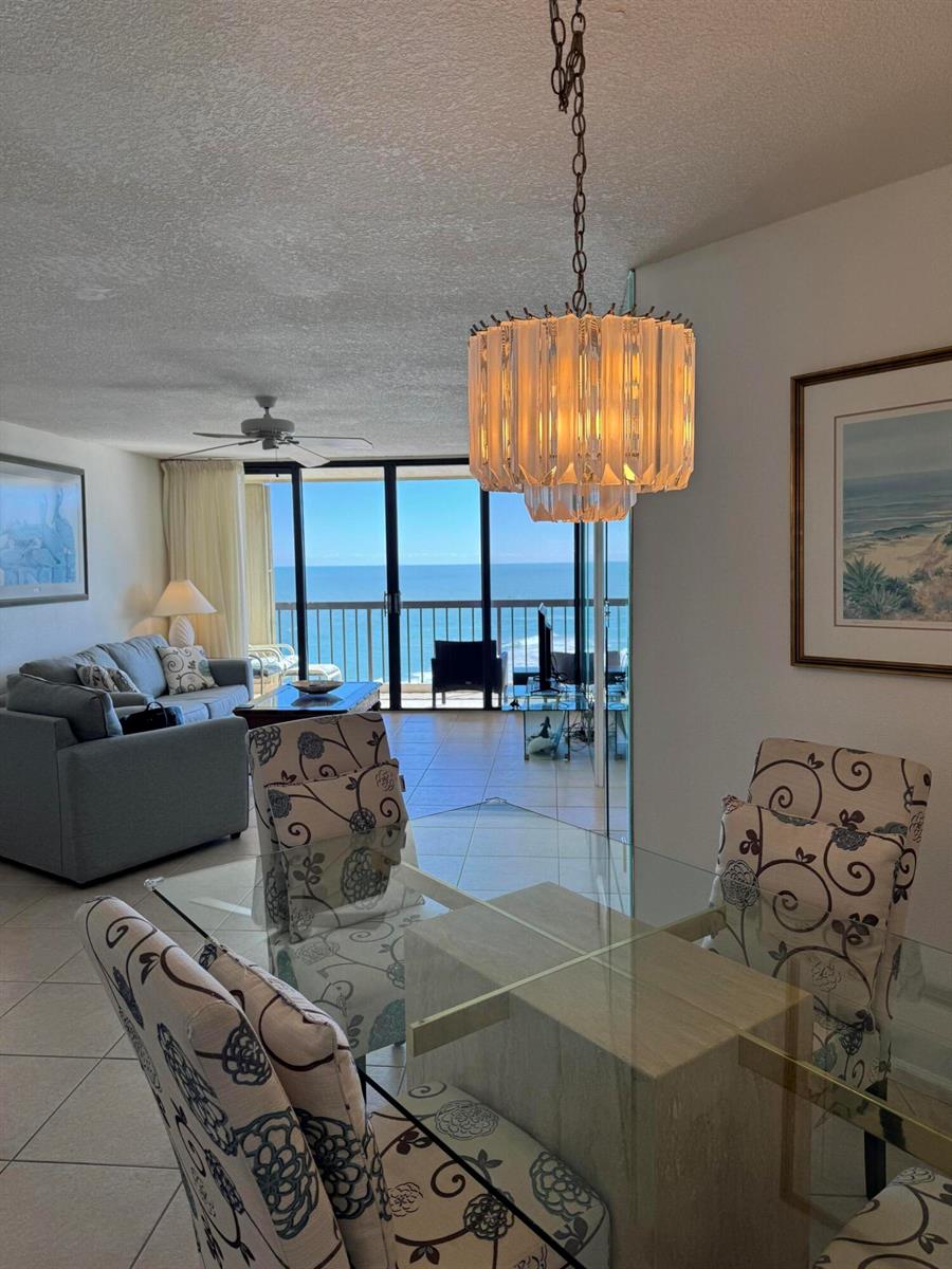 A dining area with a glass table and patterned chairs overlooks a balcony and ocean — 9500 S Ocean Drive # 09, Jensen Beach FL 34957, JENSEN BEACH, FL