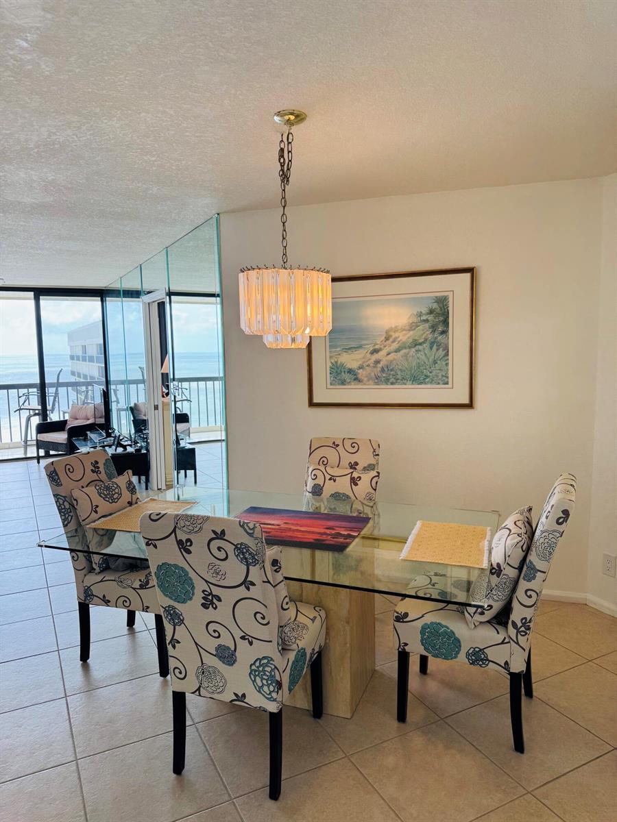 A dining area features a glass-topped table, floral chairs, and a chandelier near a balcony — 9500 S Ocean Drive # 09, Jensen Beach FL 34957, JENSEN BEACH, FL