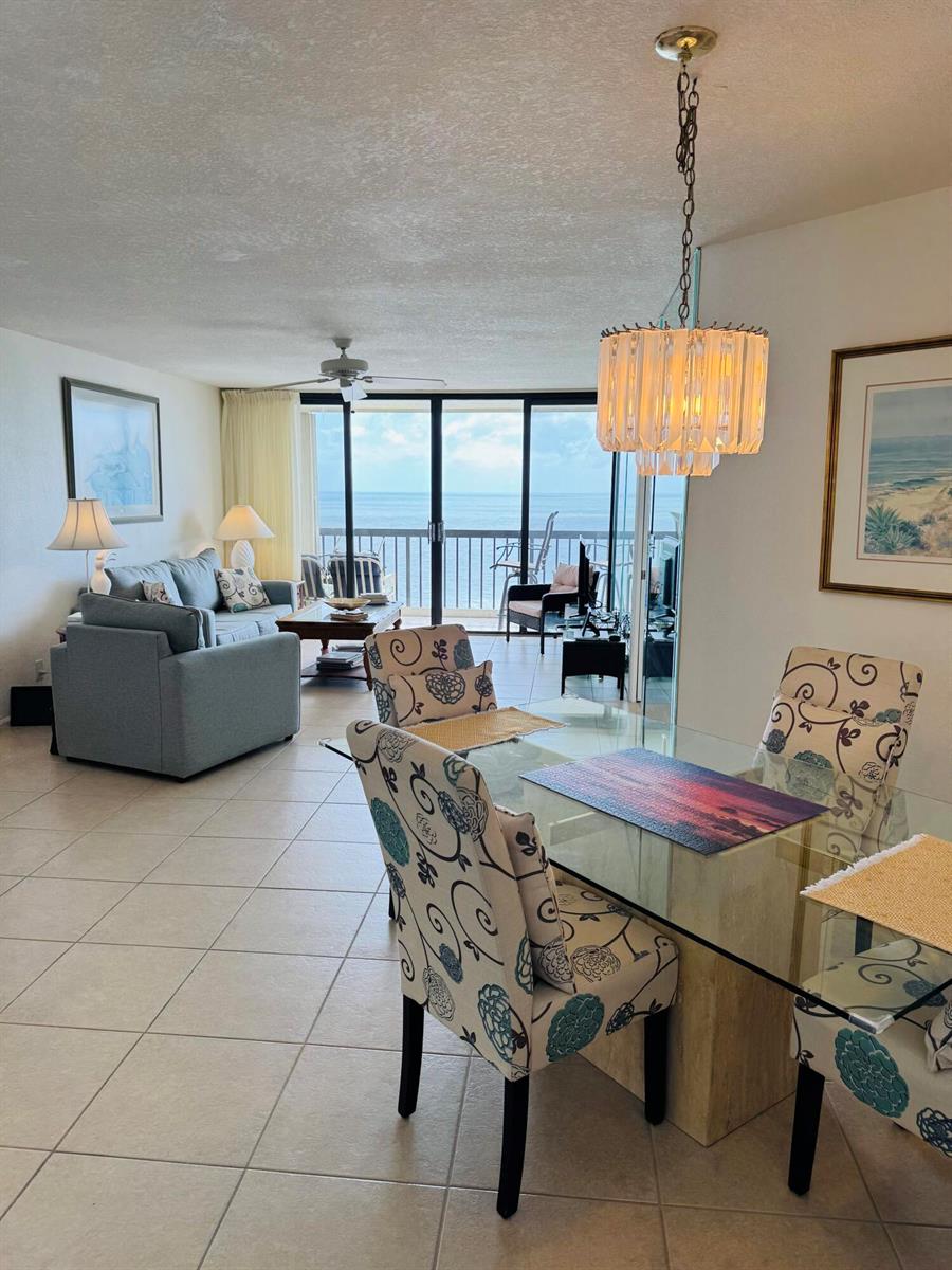 A dining area with a glass table and patterned chairs overlooks a living room and balcony — 9500 S Ocean Drive # 09, Jensen Beach FL 34957, JENSEN BEACH, FL