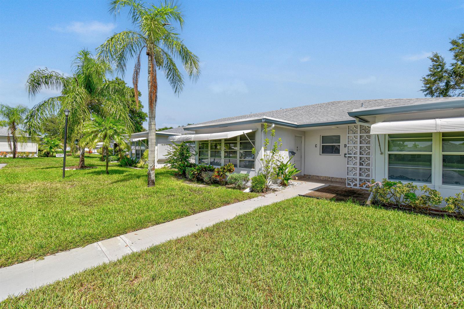A single-story residential building with a concrete walkway, palm trees, and a grassy lawn — 1097 Circle Terrace W # C, Delray Beach FL 33445, DELRAY BEACH, FL