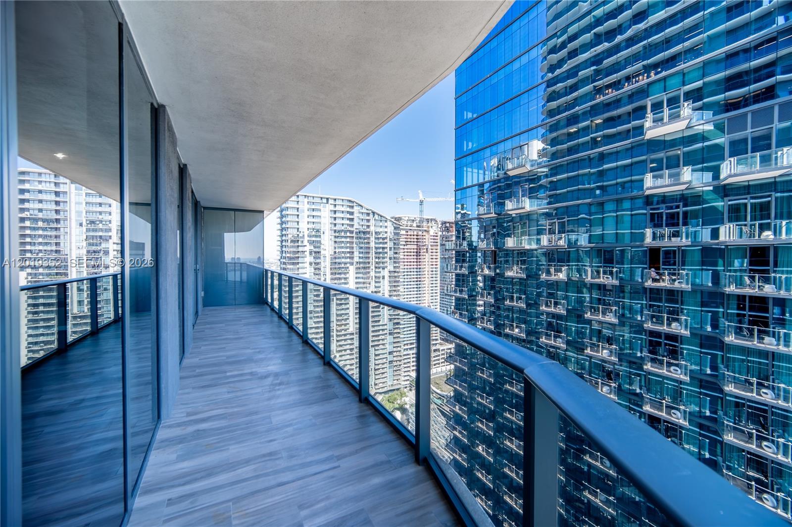 A modern balcony with wood-look tile flooring and a glass railing overlooks city skyscrapers — 801 S Miami Ave # 3905, Miami FL 33130, MIAMI, FL