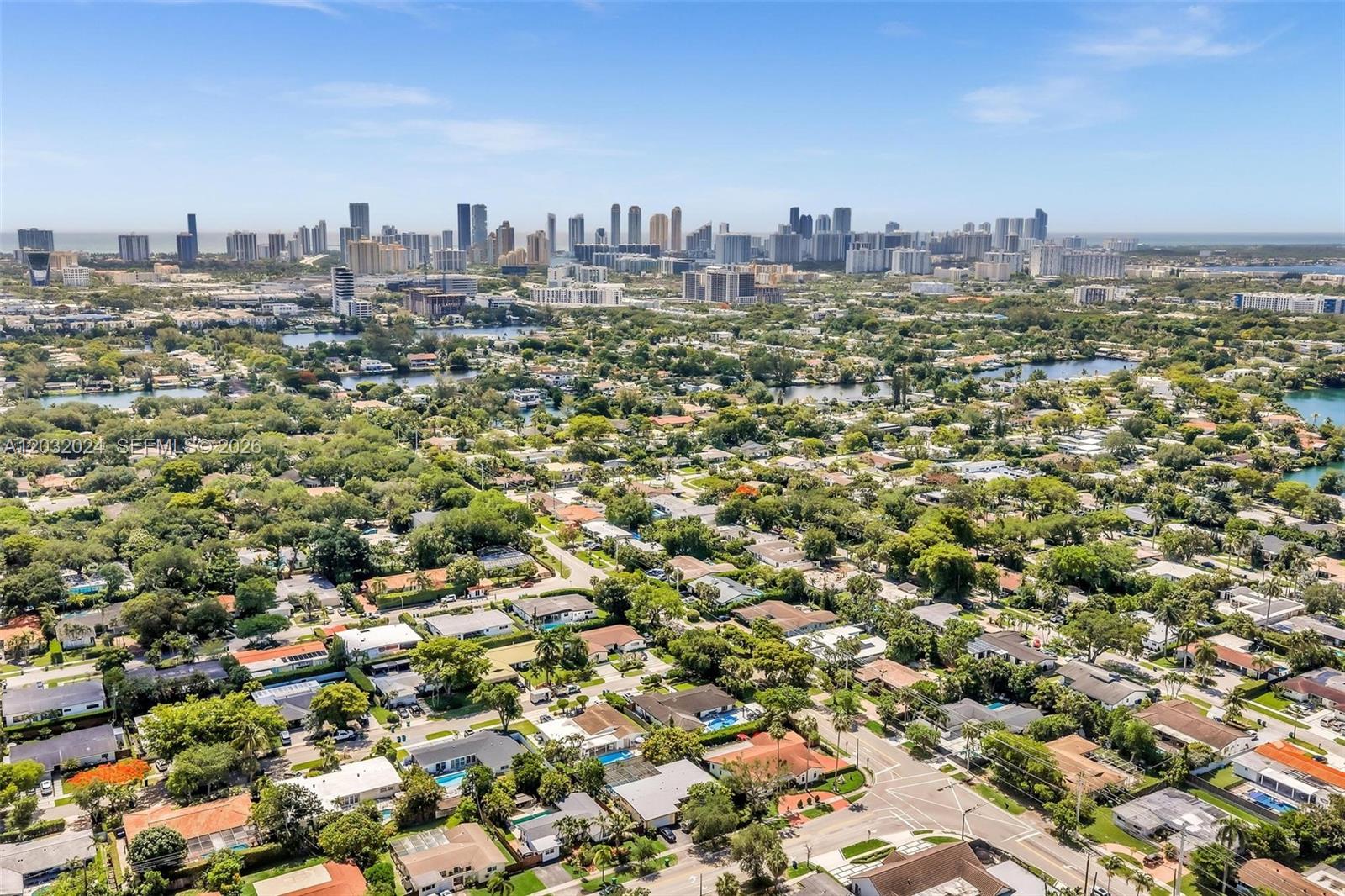 An aerial view shows a suburban neighborhood with houses, trees, and a distant city skyline — 19901 Highland Lakes Blvd, Miami FL 33179, MIAMI, FL