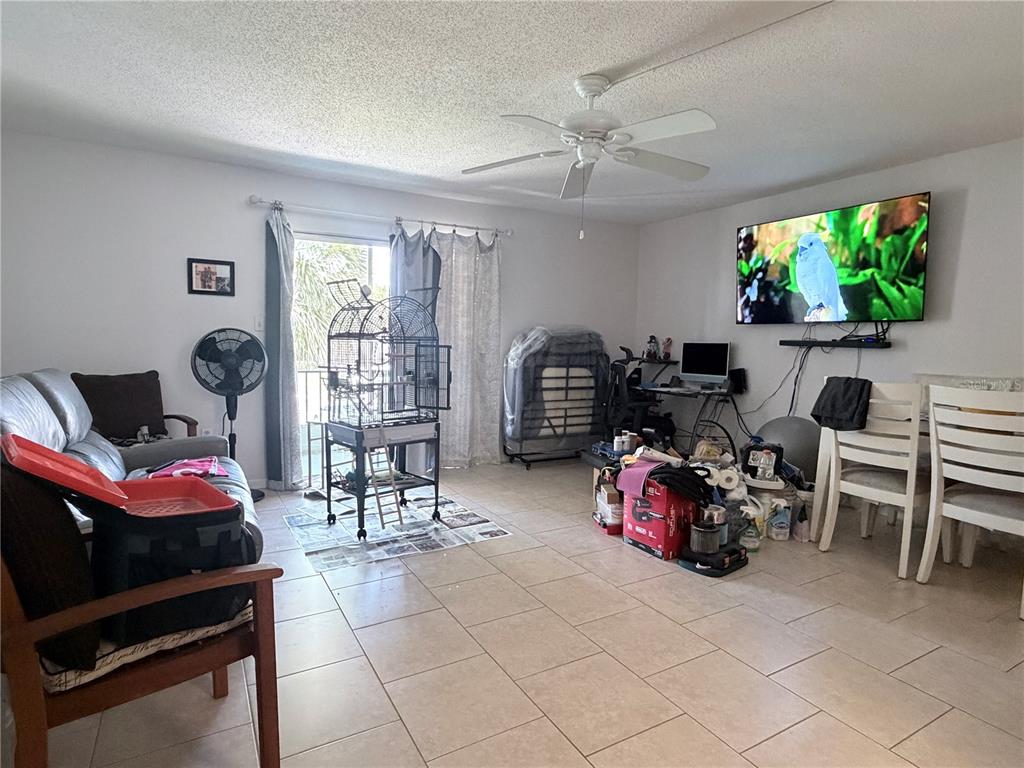 A living room with tile flooring, a ceiling fan, a birdcage, and a wall-mounted television — 2727 75TH STREET W UNIT 7A15, BRADENTON, FL