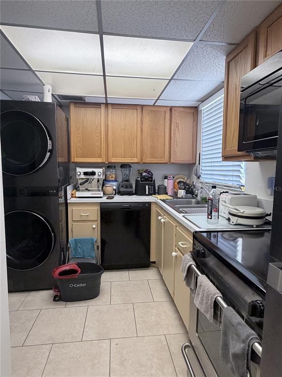 A kitchen features light wood cabinets, black appliances, a stacked washer-dryer, and tiled flooring — 2727 75TH STREET W UNIT 7A15, BRADENTON, FL