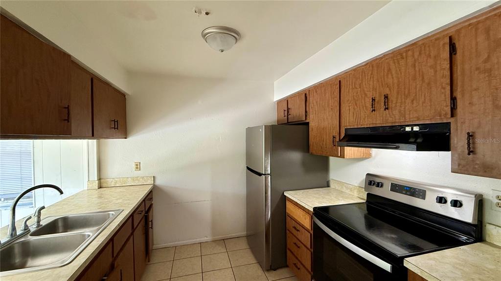 A kitchen features wood cabinets, laminate countertops, a stainless steel refrigerator, and a black stove — 202 CENTURY BOULEVARD UNIT D, AUBURNDALE, FL