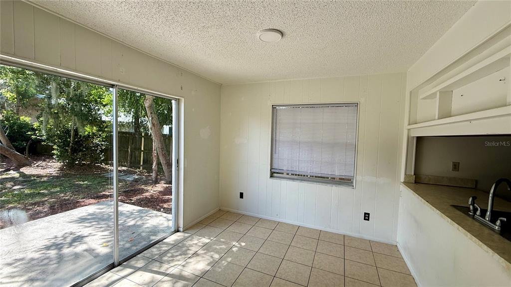 A dining area with tile flooring, wood paneling, a sliding glass door, and kitchen pass-through — 202 CENTURY BOULEVARD UNIT D, AUBURNDALE, FL