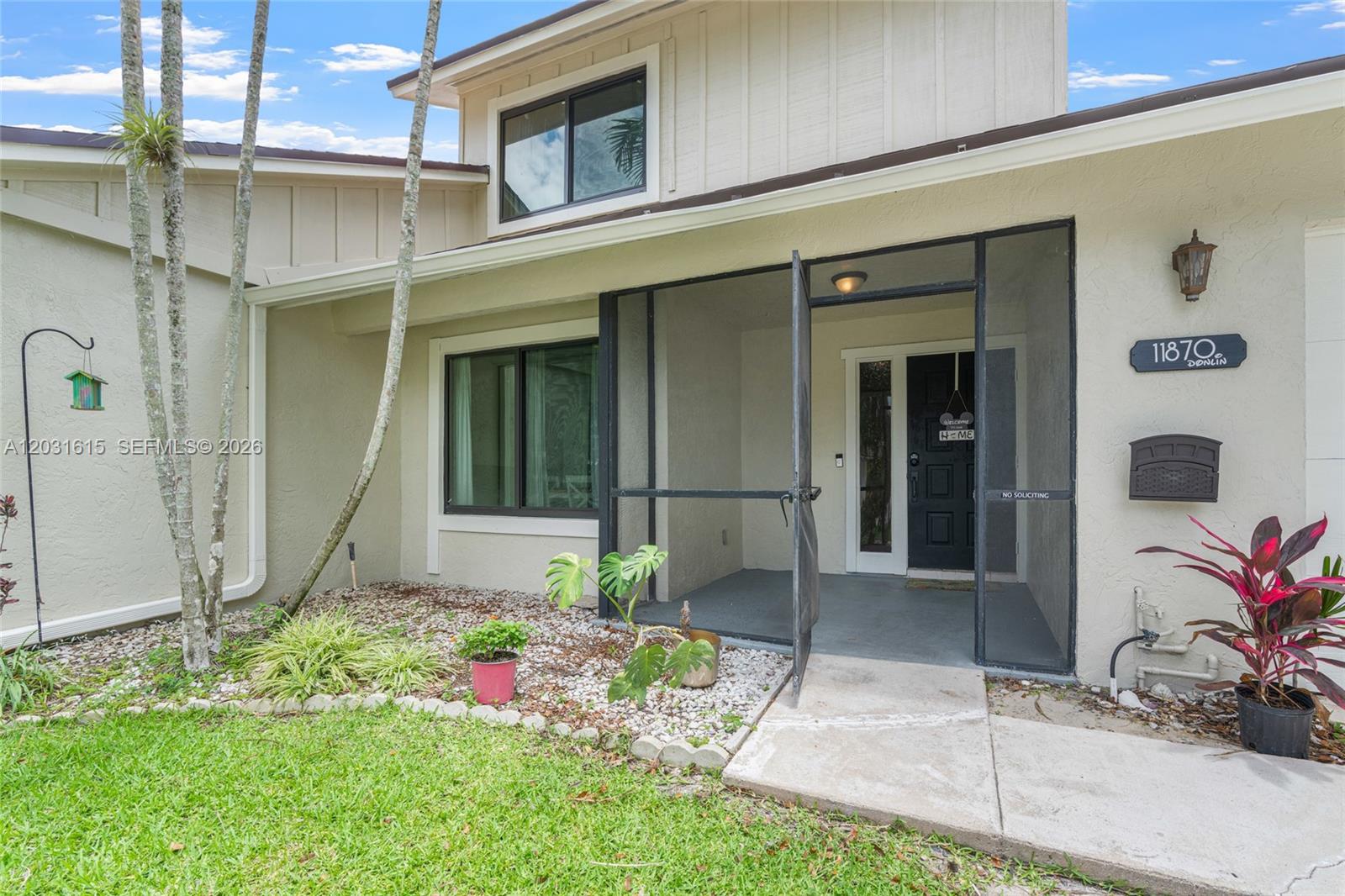 The exterior of a house features a screened-in entryway, light-colored siding, and a small front yard — 11870 Donlin Dr, Wellington FL 33414, WELLINGTON, FL