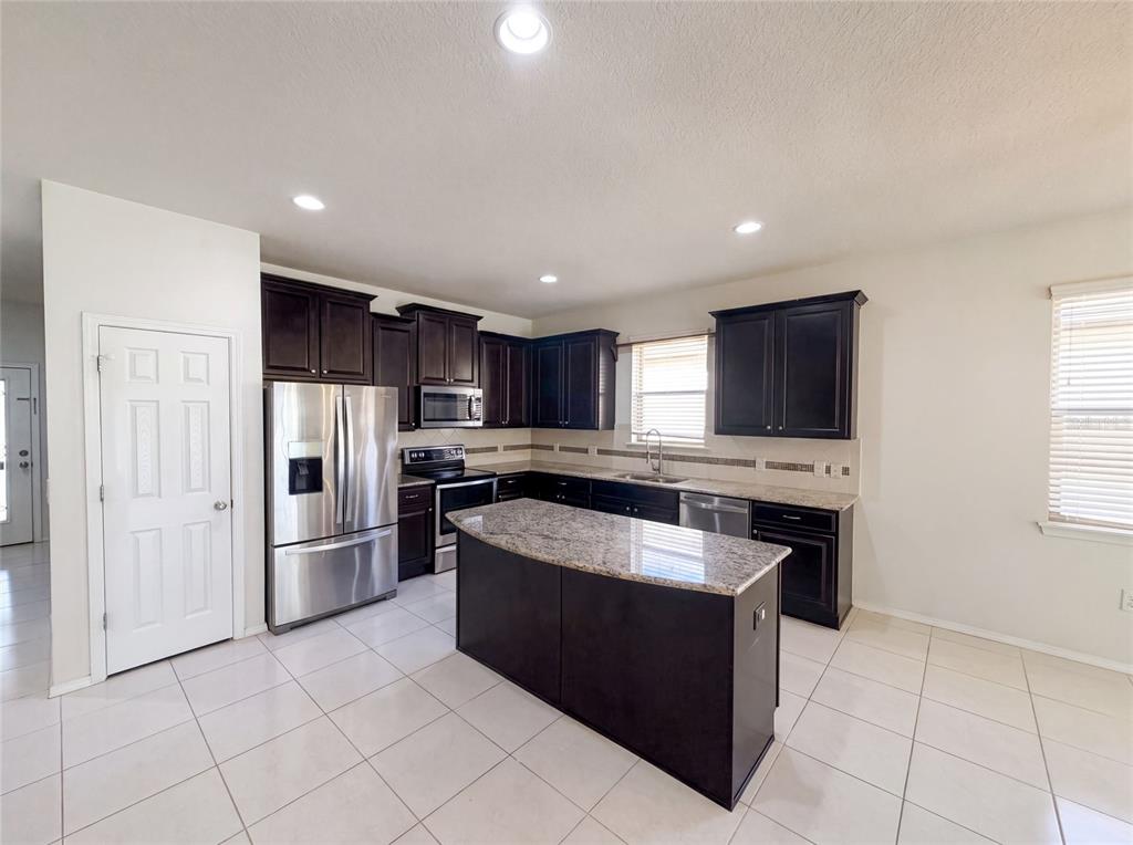 A kitchen features dark wood cabinets, granite countertops, stainless steel appliances, and tile flooring — 1857 TRILLIUM BOULEVARD, BROOKSVILLE, FL