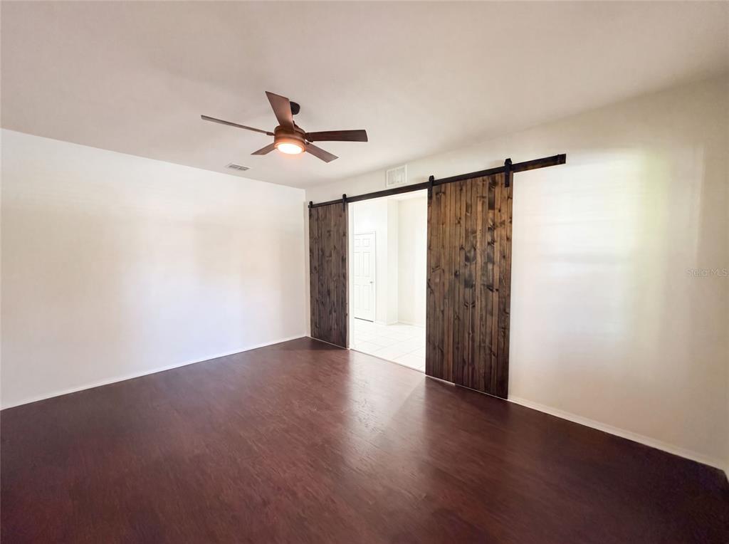 A room with dark wood flooring, a ceiling fan, and double sliding barn doors — 1857 TRILLIUM BOULEVARD, BROOKSVILLE, FL