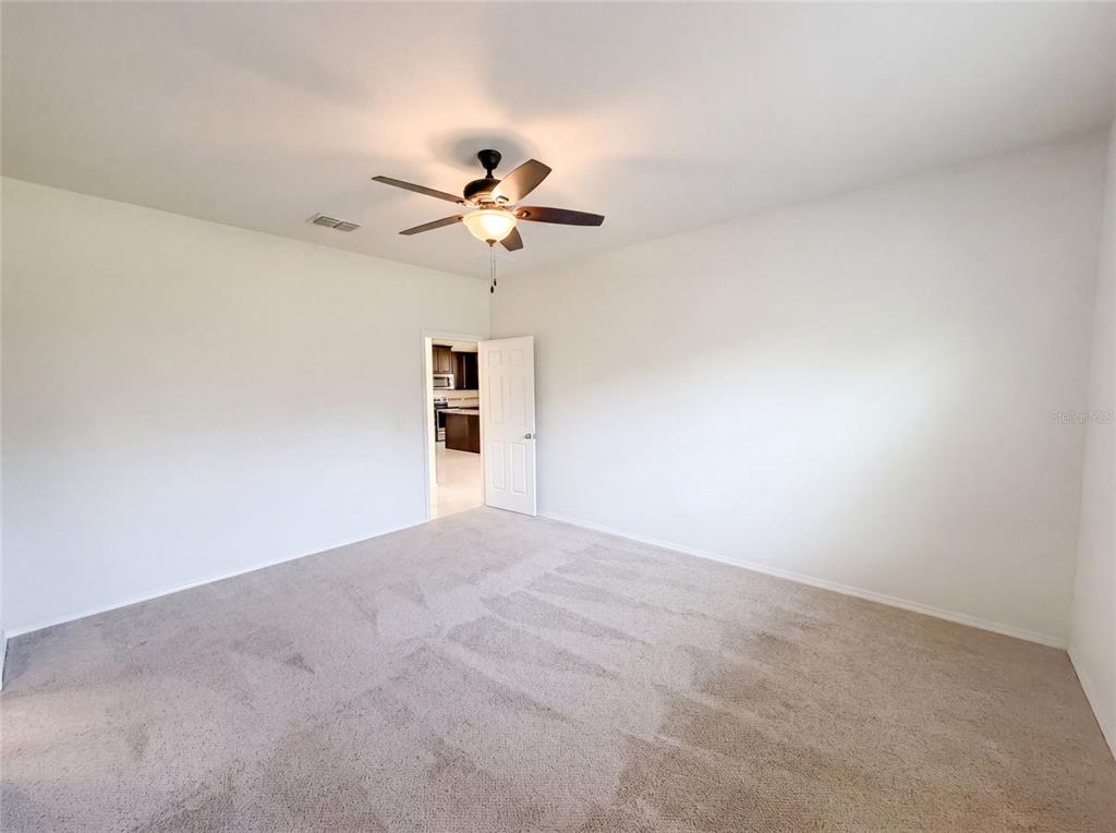 A carpeted bedroom with a ceiling fan and an open doorway leading to a kitchen — 1857 TRILLIUM BOULEVARD, BROOKSVILLE, FL
